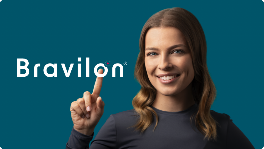 Usmívající se žena v tmavém tričku s dlouhým rukávem ukazuje na logo Bravilon®, symbolizující sebedůvěru a účinnou léčbu oparu; písmeno „o“ na špičce jejího prstu symbolizuje tabletu umístěnou na konečku prstu.